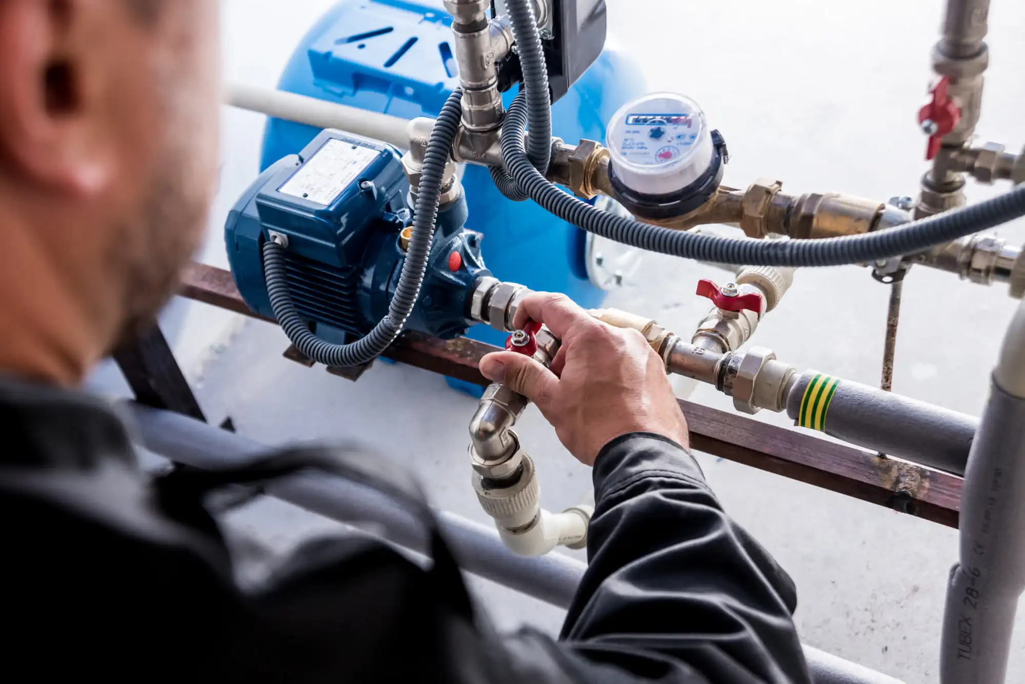 A technician adjusting a valve on a constant pressure pump, tank, and water meter assembly