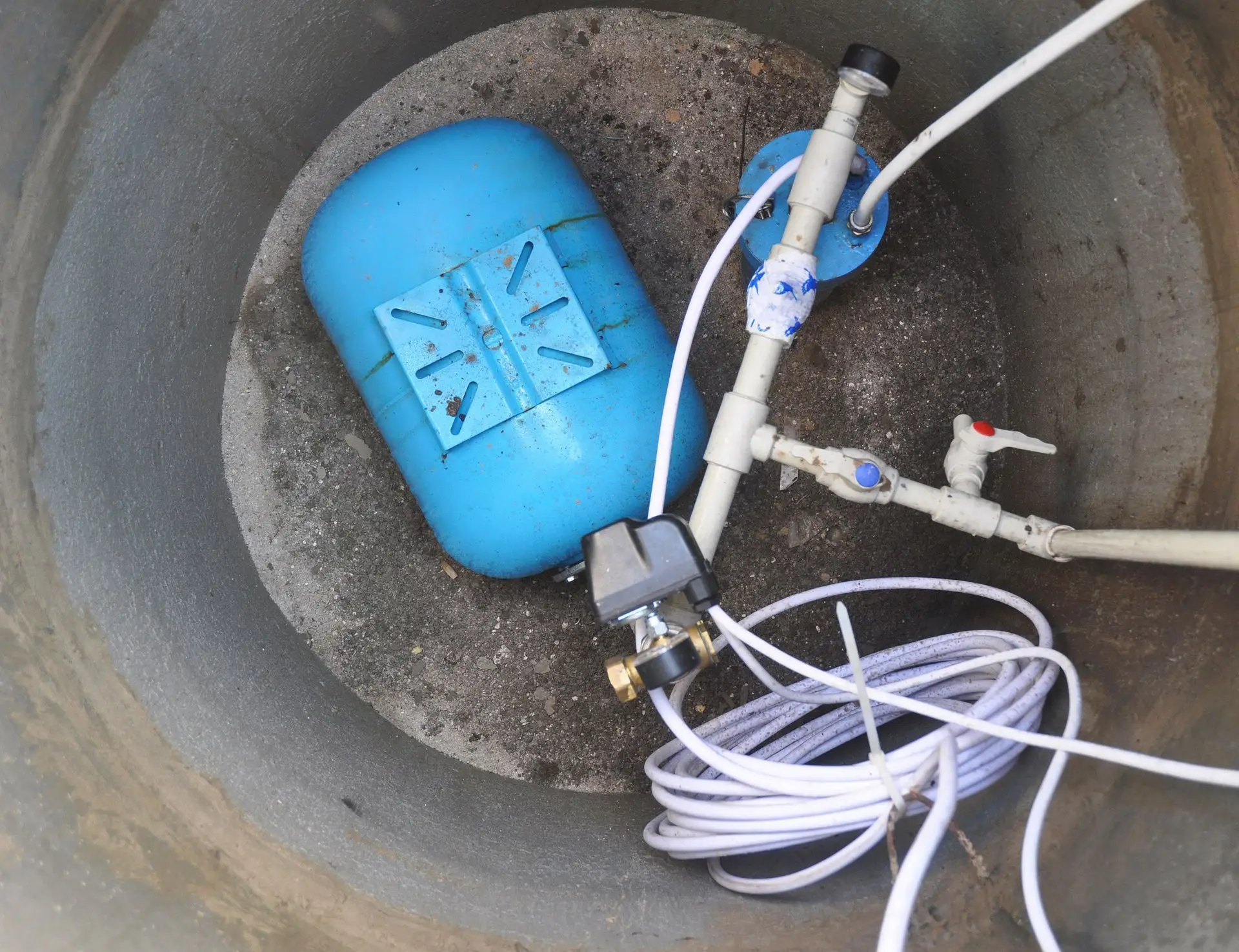 A water pump with white cables is placed at the bottom of a small well.