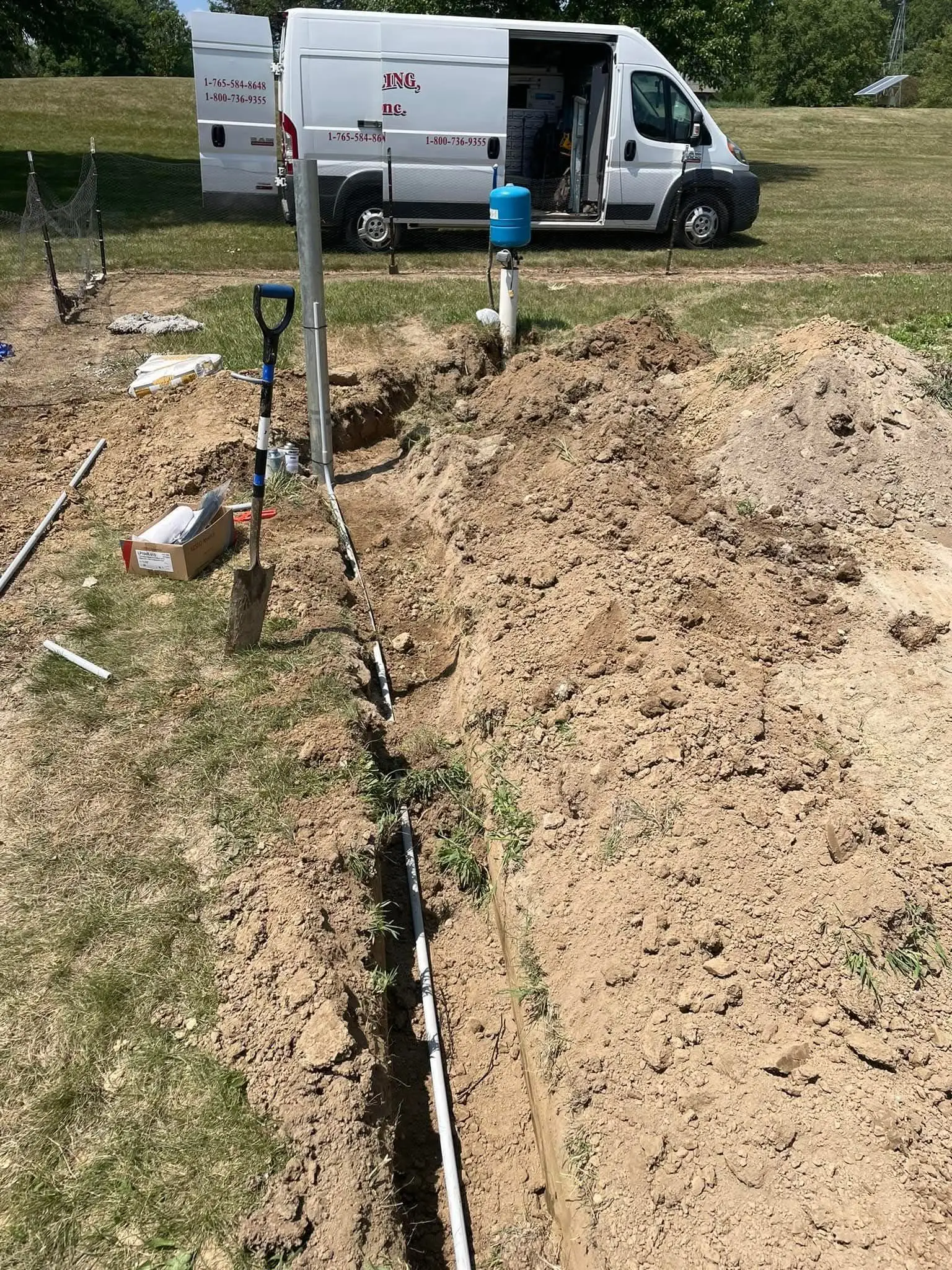 A Wiley Well Drilling service van beside a trench with newly installed water line and pressure tank.