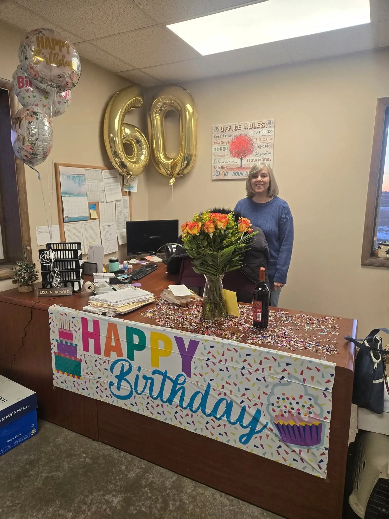 A person standing behind an office desk decorated with balloons and a Happy Birthday banner.