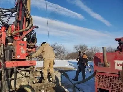 Drillers working beside a red rig on a snow-covered job site under a blue sky