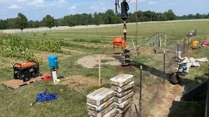 Auger drilling rig boring a new well in a farm field with grout bags staged nearby