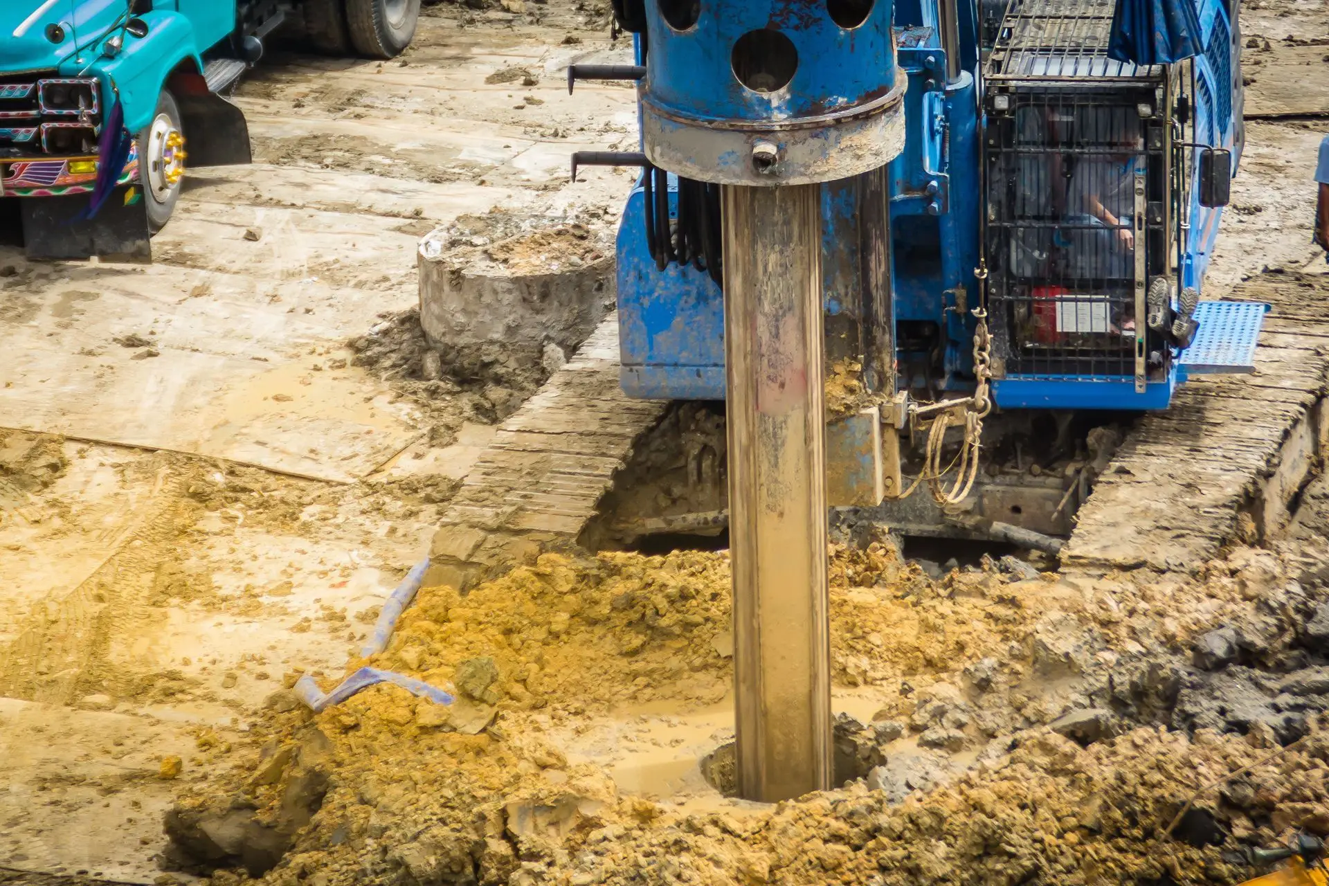 Blue rotary drilling rig bores deep into wet, sandy soil at an active water well replacement site.